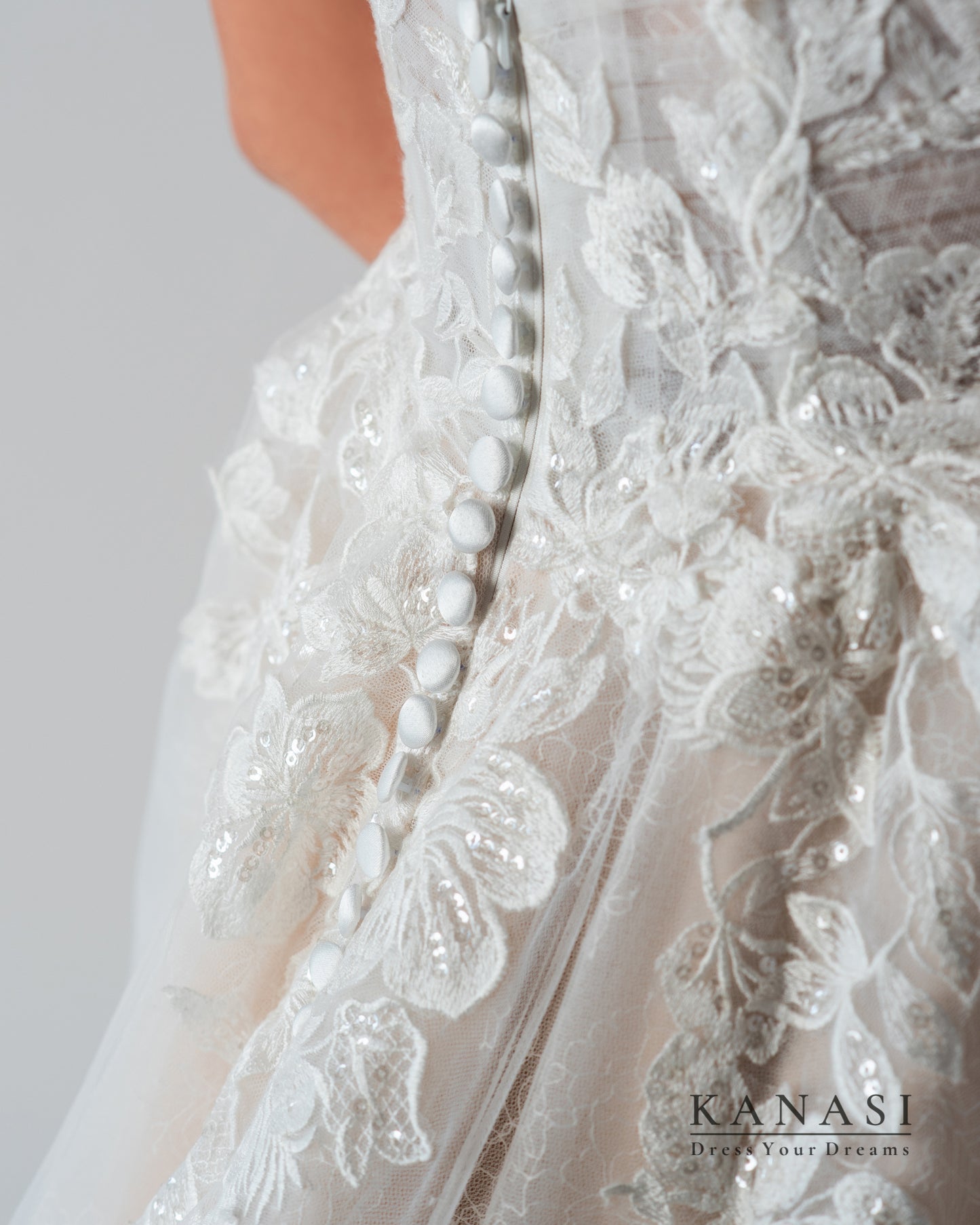 Detajl hrbtnega dela poročne obleke s čipko in okrasnimi gumbi.